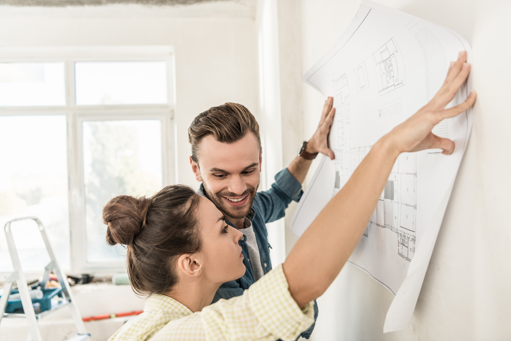 Couple holding blueprint at wall during home improvement project.